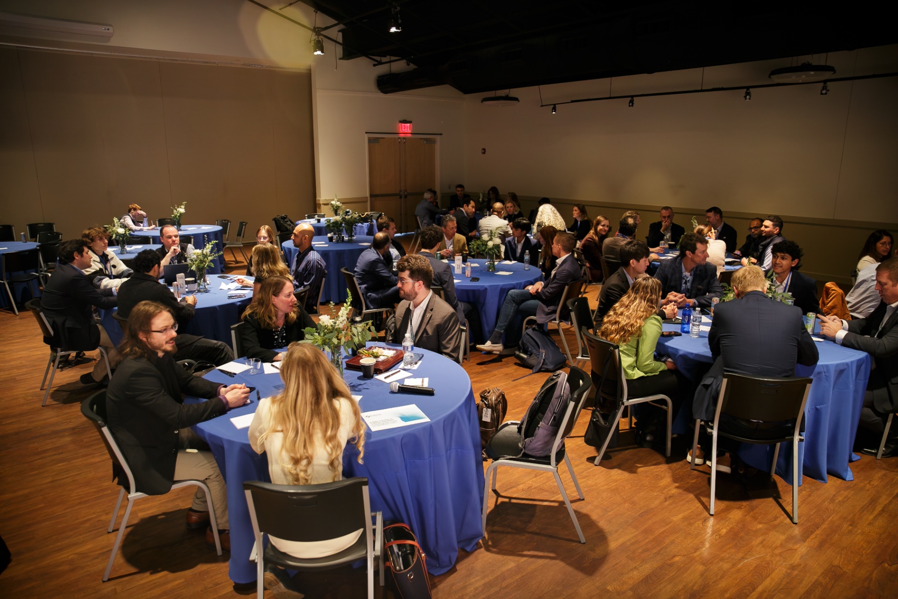 Full room of attendees at curated roundtable dinner tables